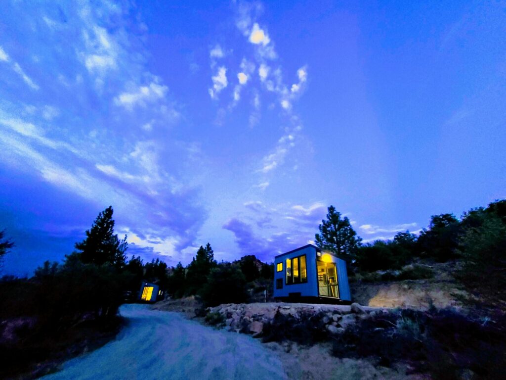 High Camp cabins glowing against a dramatic dusk sky surrounded by pines