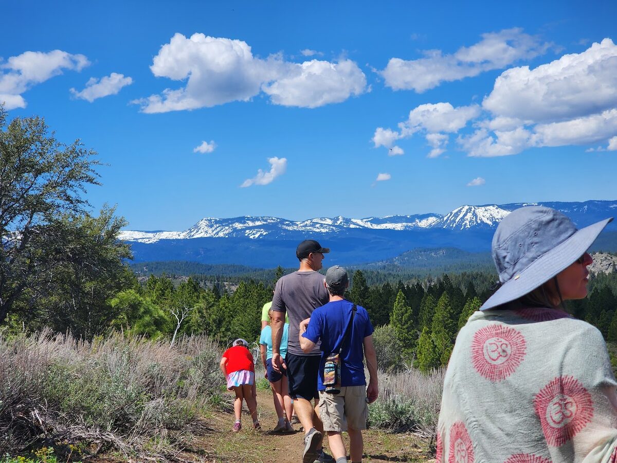Hikers on a trail near Beckwourth Peak with snow-capped mountains and blue sky behind them